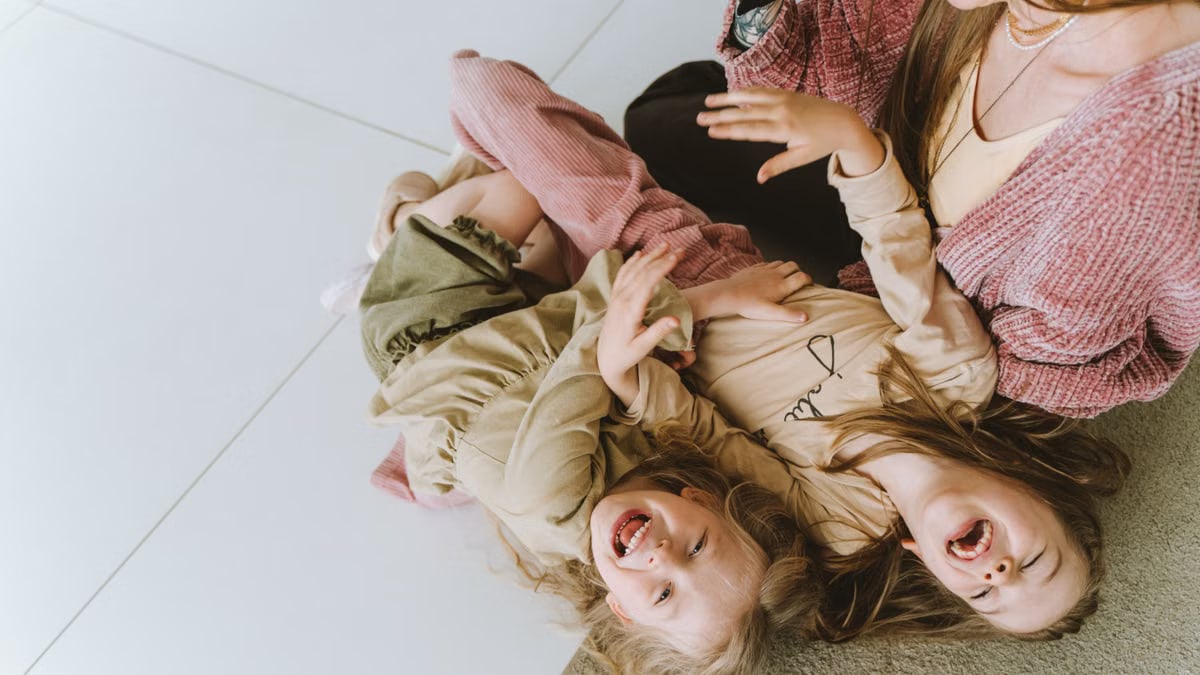 Mother and daughters laughing and bonding on the floor, capturing joyful family moments.